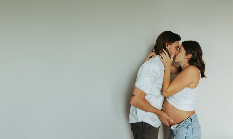 Pregnant Couple Sharing Intimate Kiss Against Minimal Wall