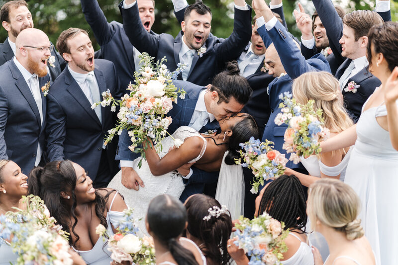 couple kissing in group photo on wedding day