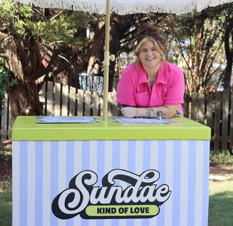 woman smiling, leaning over a striped ice-cream cart.