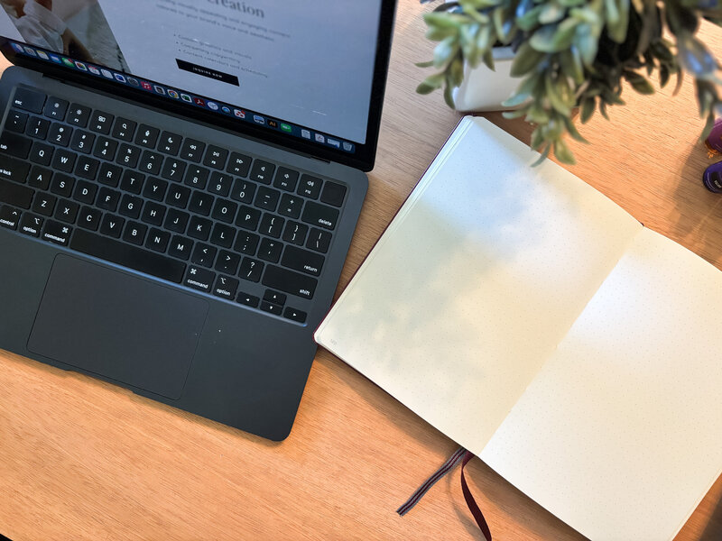 Top view of open laptop and empty notebook with plant, essential oils, and cozy workspace vibe