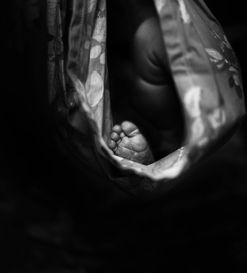 A black and white newborn photo of a baby's foot while the baby is inside of a swaddle cloth
