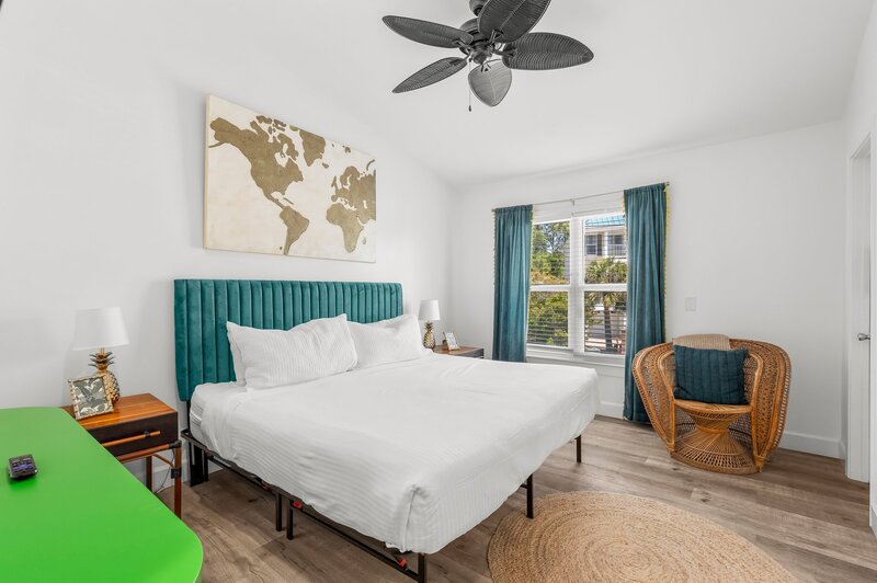 Upstairs king bedroom with large windows, rattan accents, and tropical touches at Tropical House in Panama City Beach, FL.