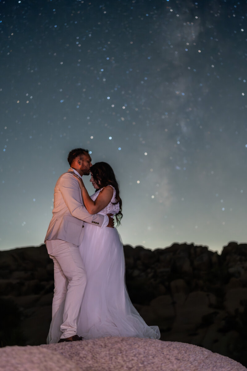 Joshua Tree Elopement Bride and Groom portrait at Jumbo Rocks Campground kissing during night stars with milky way.