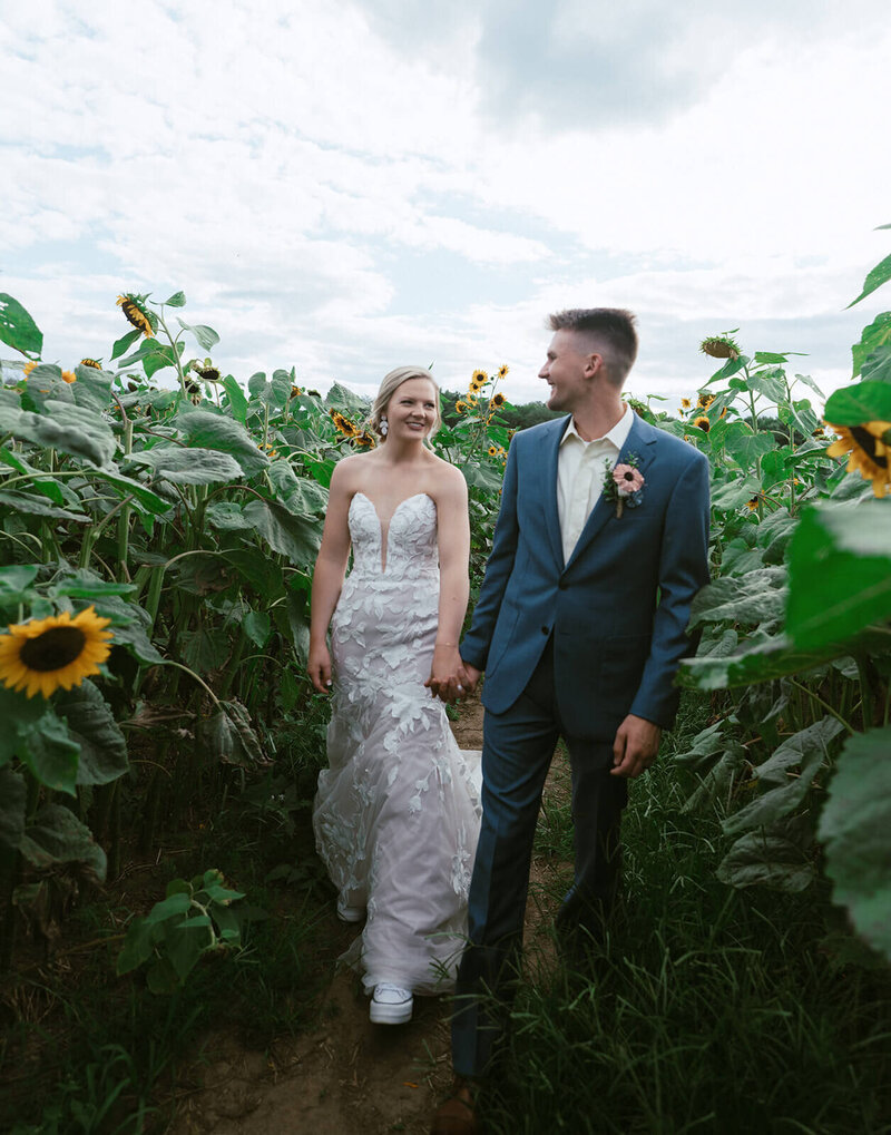 The groom and bride are walking hand in hand amidst the sunflowers.
