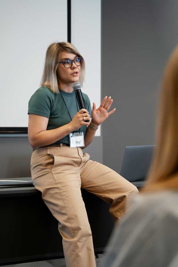 Woman leaning against desk speaking in a microphone
