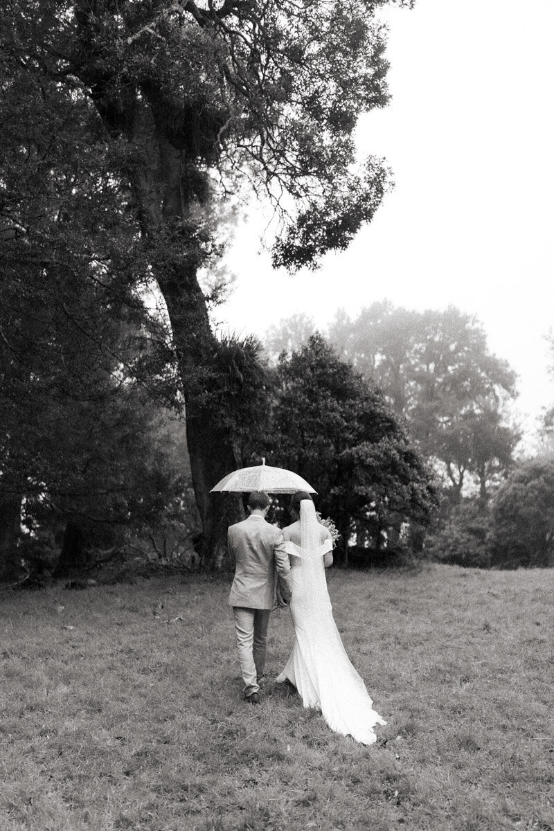 A black and white portrait of a wedding couple in the rain on their farm. Captured by Eilish Burt Photography