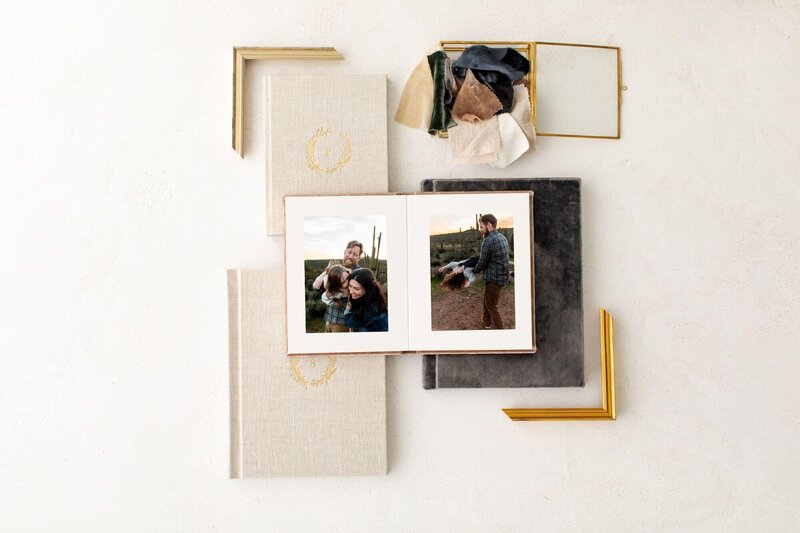album with accent details surroundingalbum with 2 maternity portraits taken by Cactus & Pine Photography, laying open on top of three other albums and 2 golden frame corners and a glass box with swatches surrounding it in an artistic way
