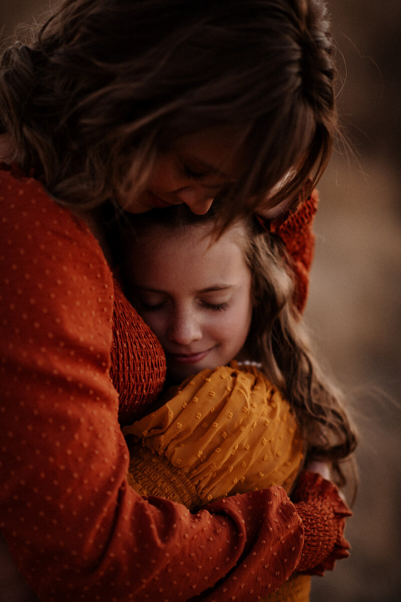 A mother and daughter in an embrace with eyes closed in a field in Gillette WY