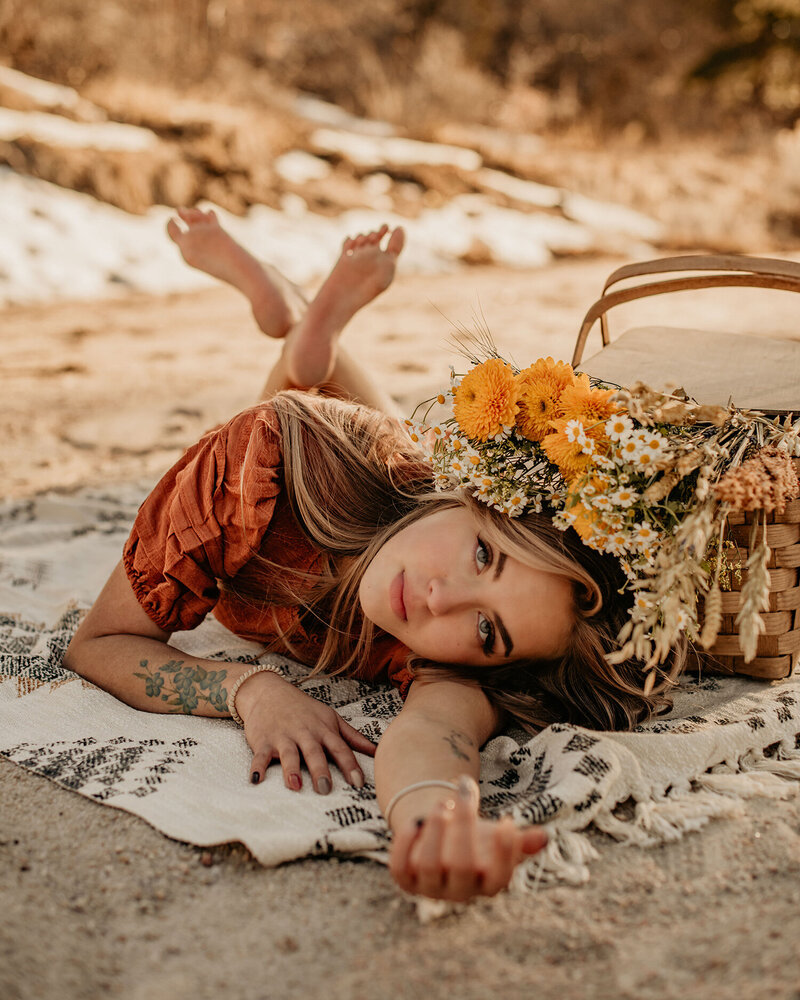Senior model laying in sand with basket of flowers.