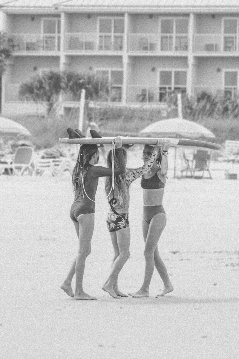 Three surfer girls carry longboard together in Jacksonville Beach, Florida