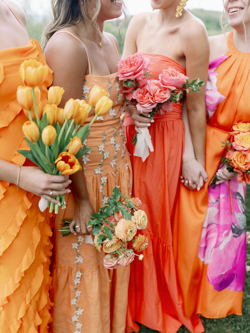 Bridesmaids in mismatched colorful gowns with monochrome flowers for a destination wedding in the mountains at Cedar Lakes Estate