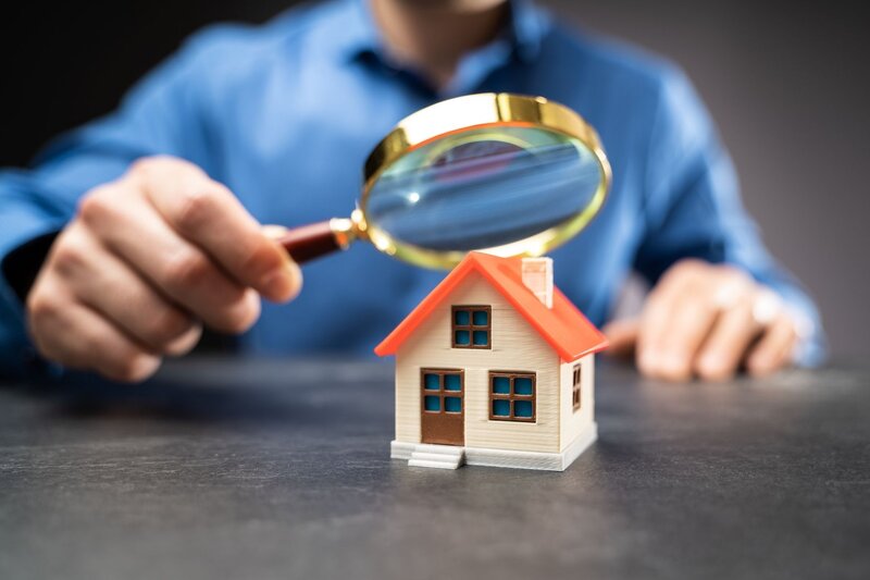 man holding magnifying glass over a house showing an inspection visual