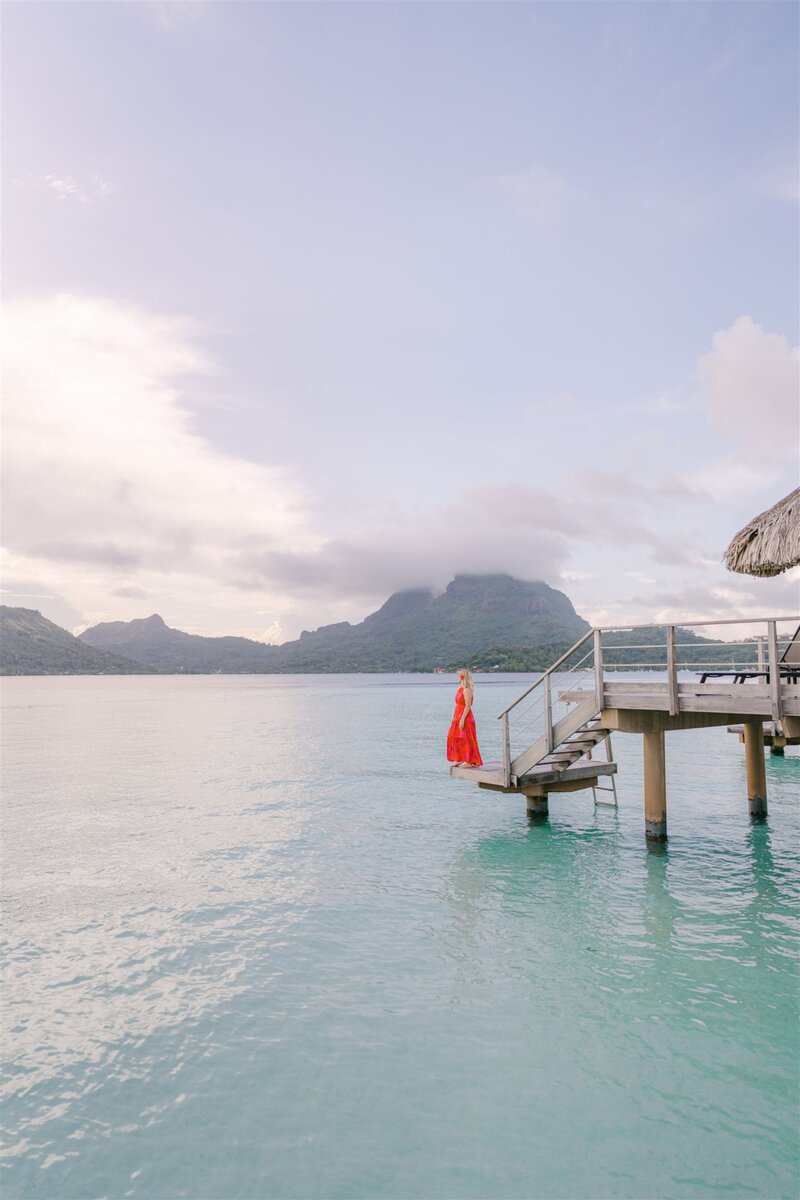 A person stands on the edge of Overwater bungalows and a peaceful lagoon view in Bora Bora at sunset