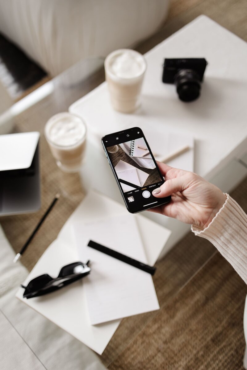 Hunted Aesthetic Team member taking photo of laptop and coffees with paper work on clear table