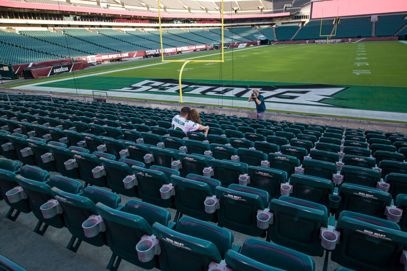 Engaged couple in the stands at Lincoln Financial Field during an Eagle-themed engagement session, capturing a behind-the-scenes glimpse filled with team spirit and love in an iconic sports venue.