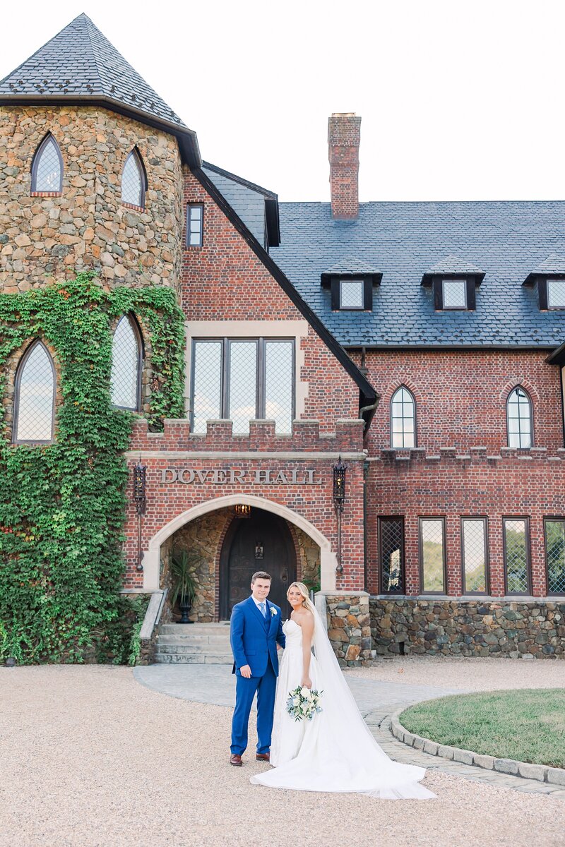 Bride and groom standing together in front of the grand stone façade of Dover Hall, surrounded by lush gardens and elegant architecture, sharing a joyful moment on their wedding day