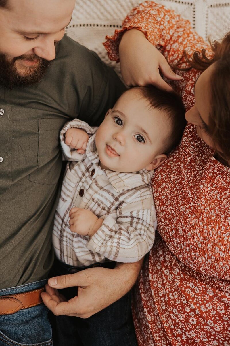A smiley, brown-eyed baby boy is nestled in between his mother and father for a family photoshoot in Oklahoma City