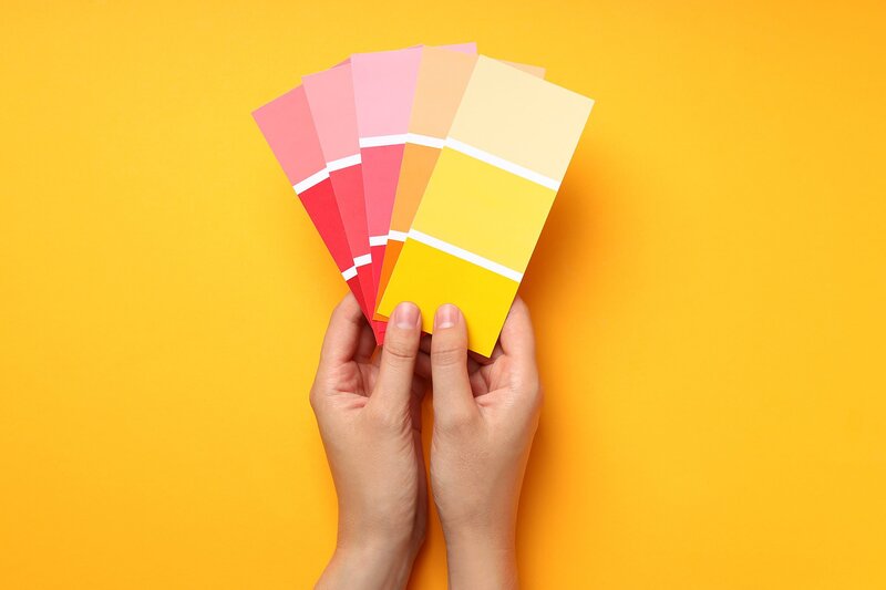 Two hands holding up color swatches on a yellow wall