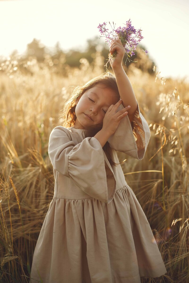A young girl standing peacefully in a field holding flowers, representing calm, focus, and the self-regulation support offered by Pacific Kids Occupational Therapy in Orange County.