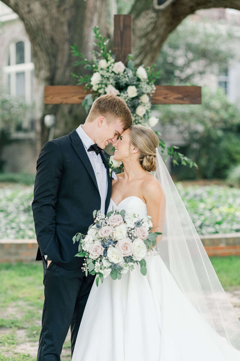 rid eand groom standing in front of a cross touching foreheads