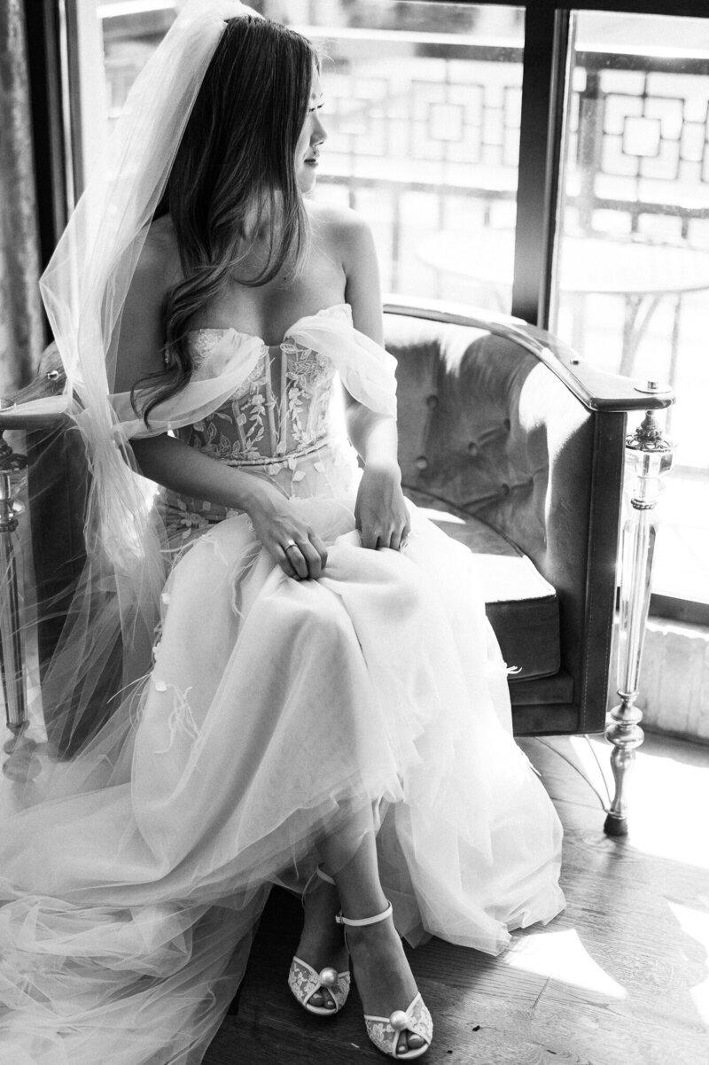 bride dressed in bridal gown & veil sitting on chair looking out the window