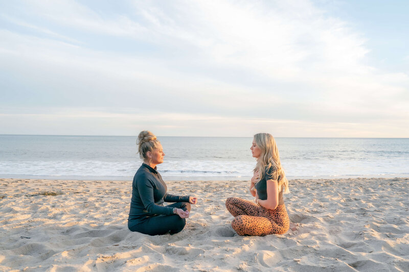 A woman life coach sitting on the beach across from her client in a meditative breathwork session in Malibu California.
