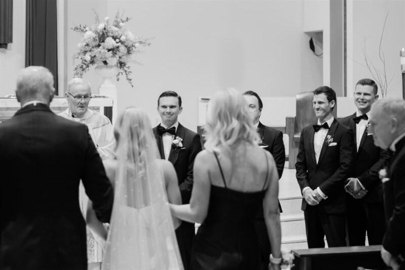 Black and white photo of a groom watching his bride walk down the aisle at a Catholic Church in Winter Park. 