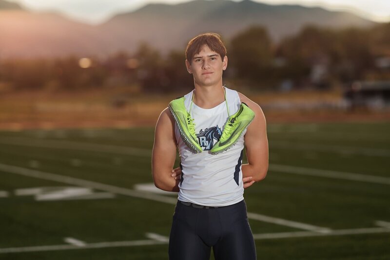 Senior posing with his cleats on high school track at his denver senior photographer session.