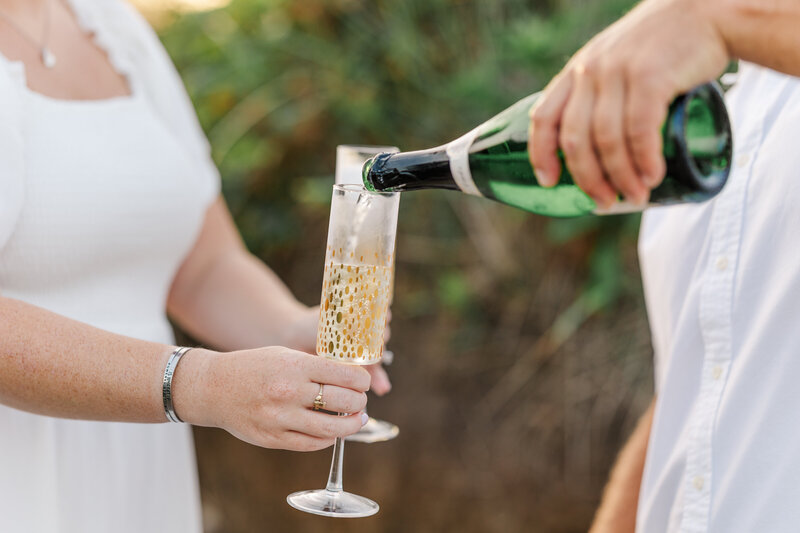 groom pouring champagne into glasses for engagement shoot champagne toast