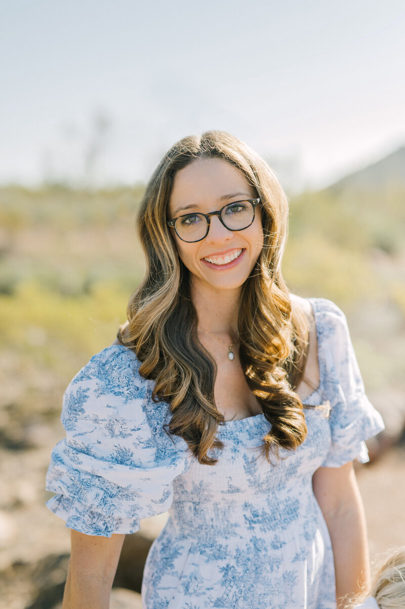 Dallas photographer smiling big wearing a blue and white print dress outside.