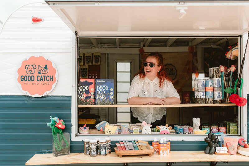 Zoe Gottstein smiling at Good Catch pop-up trailer window, showcasing pet treats and toys.