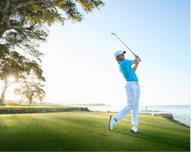 Man swinging a golf club at a scenic oceanfront course in the Dominican Republic