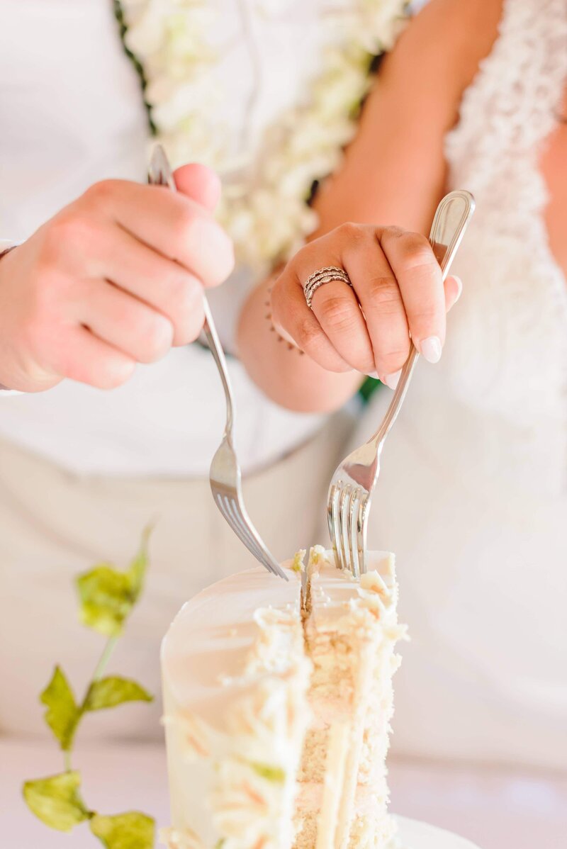 Two forks dig into a wedding cake.