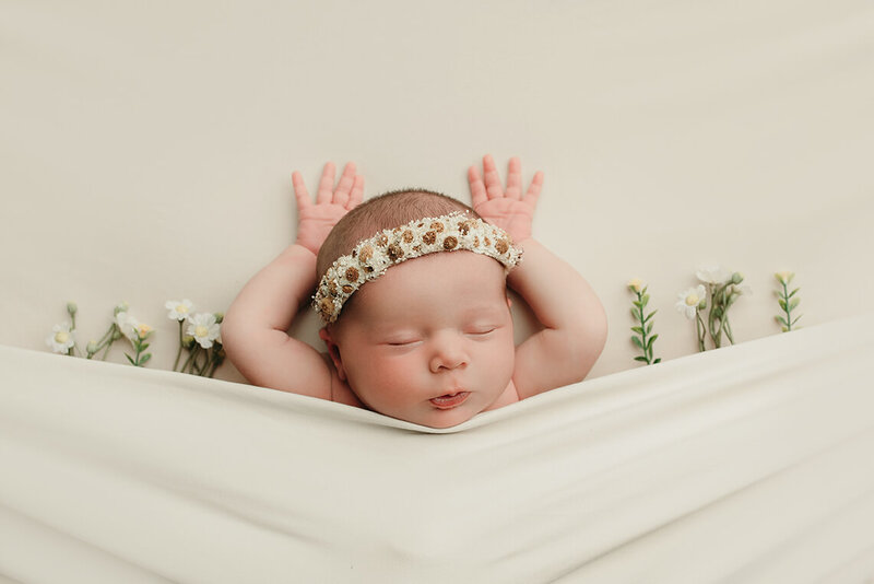 a newborn girl laying on her back with her hands above her head laying with daisies
