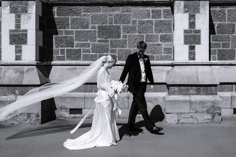 a bride and groom walk past the christchurch arts centre brickwork on their urban christchurch wedding day