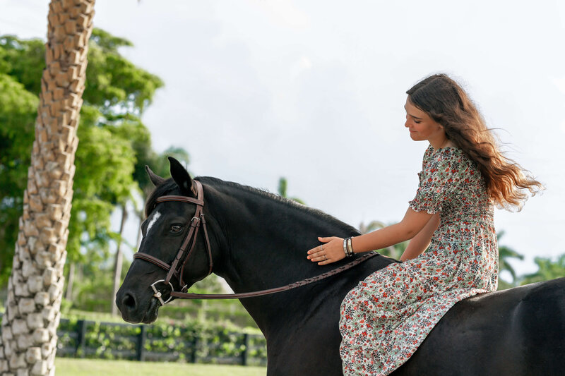 tallahassee florida equine photography of a girl in a sundress sitting on her horse's back patting its neck