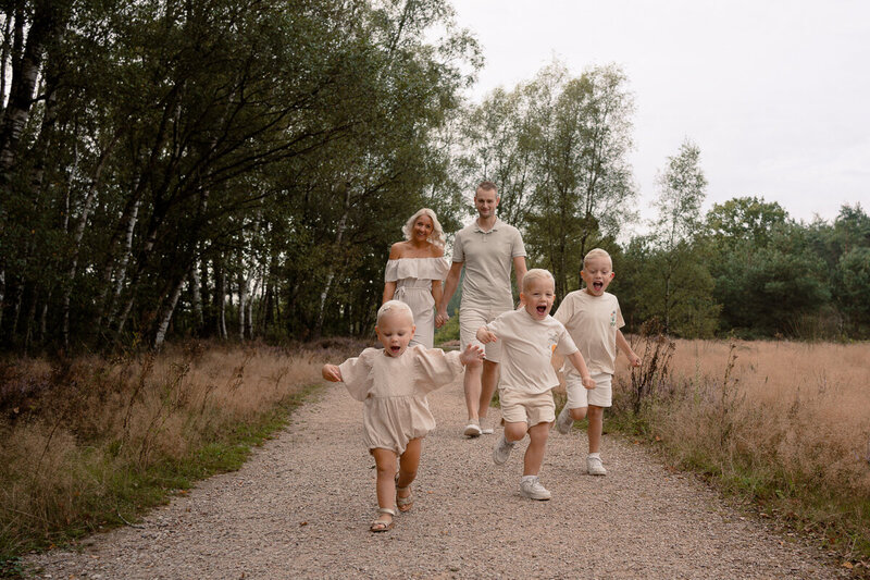 Ouders lopen hand in hand terwijl hun drie kinderen lachend voor hun rennen.