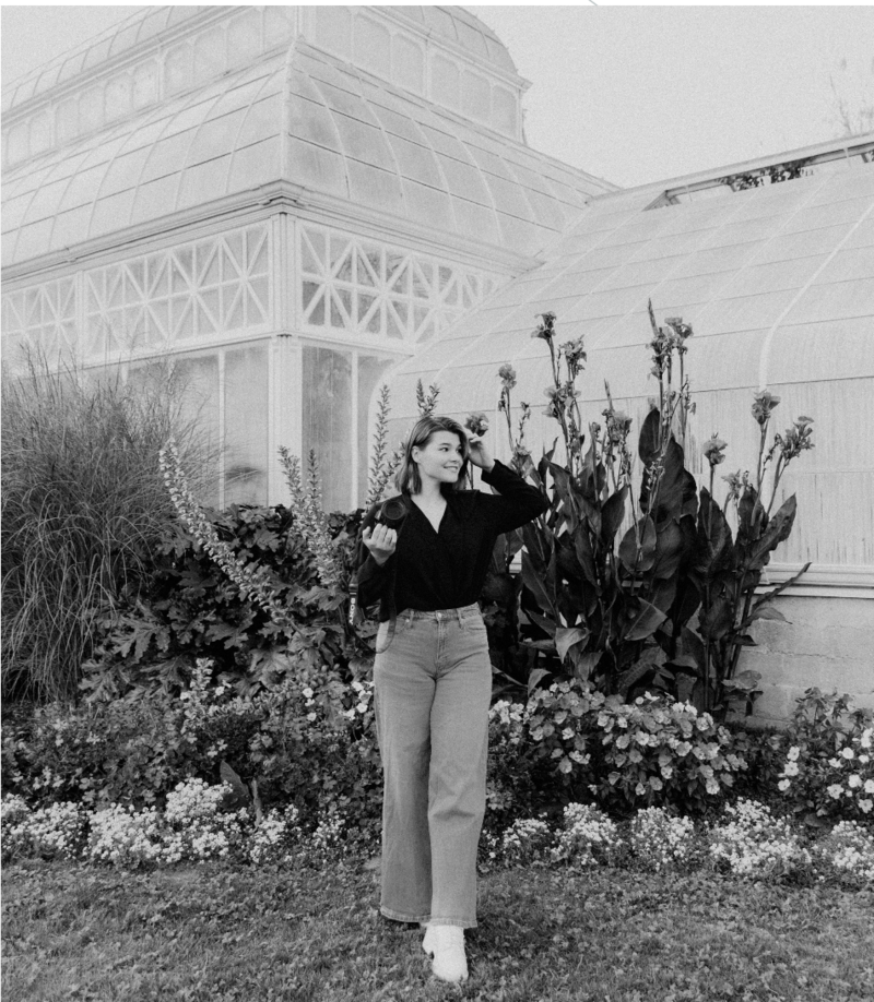 woman standing in front of greenhouse holding camera