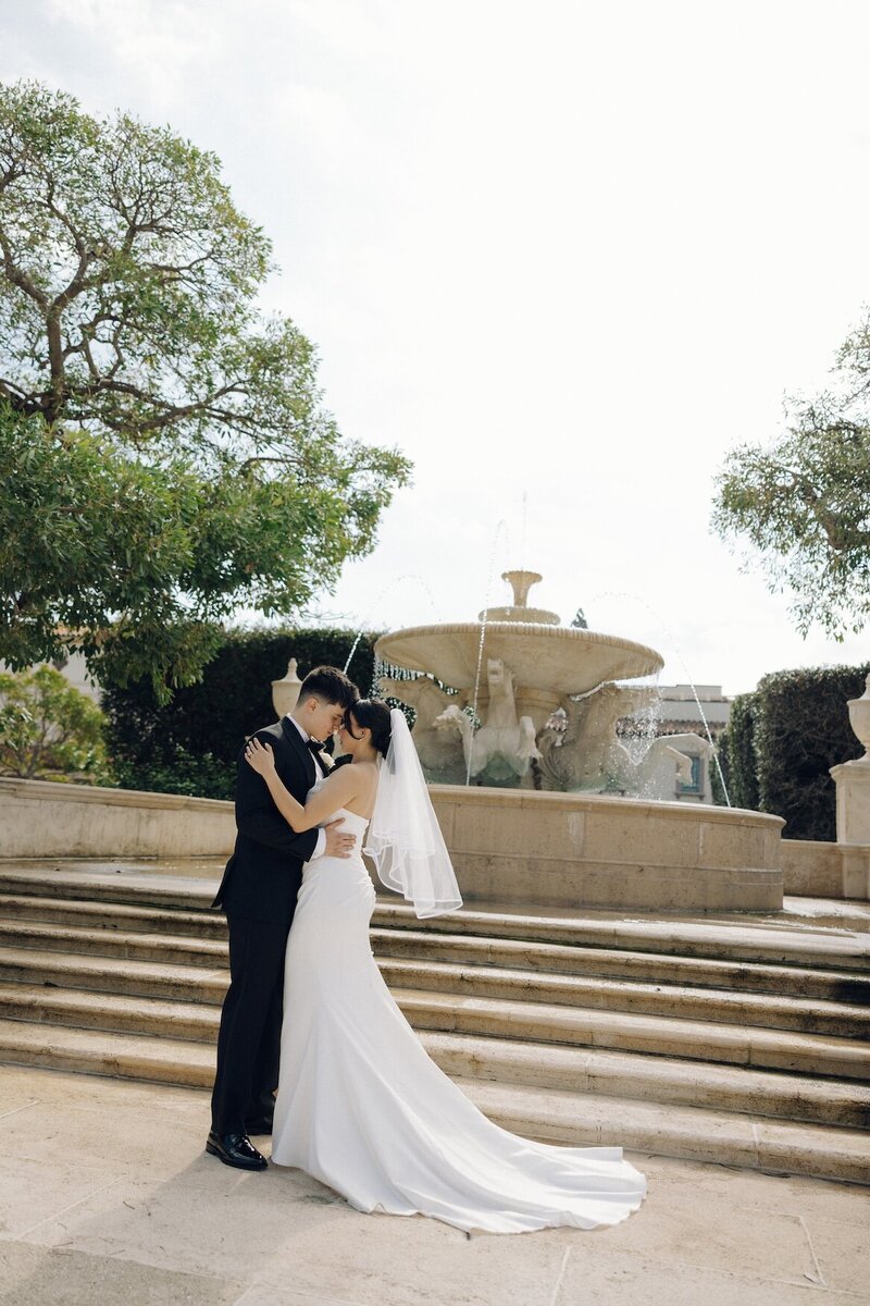 bride and groom embrace in front of fountain after wedding