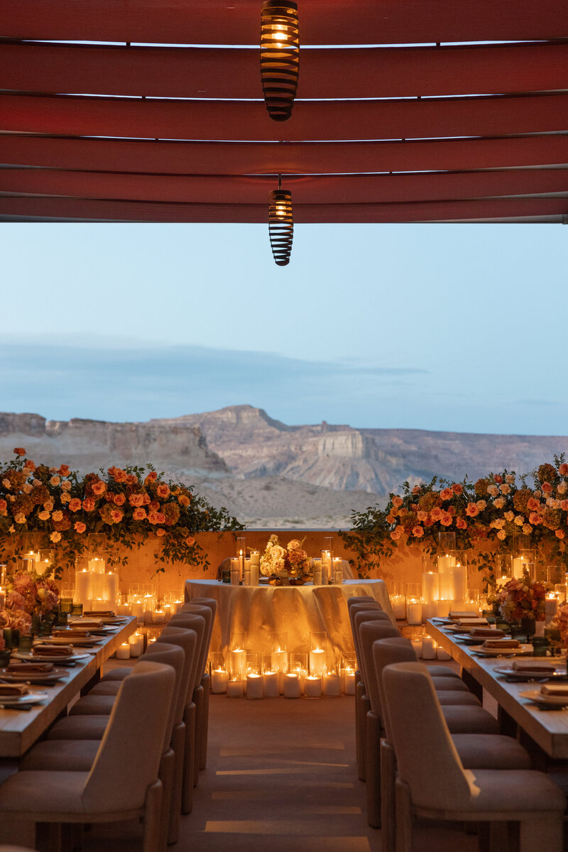 An outdoor wedding reception at Amangiri in the Mesa Breezeway with a panoramic view of the mountains behind a sweetheart table. Oversized candles glow and neutral roses frame the view.
