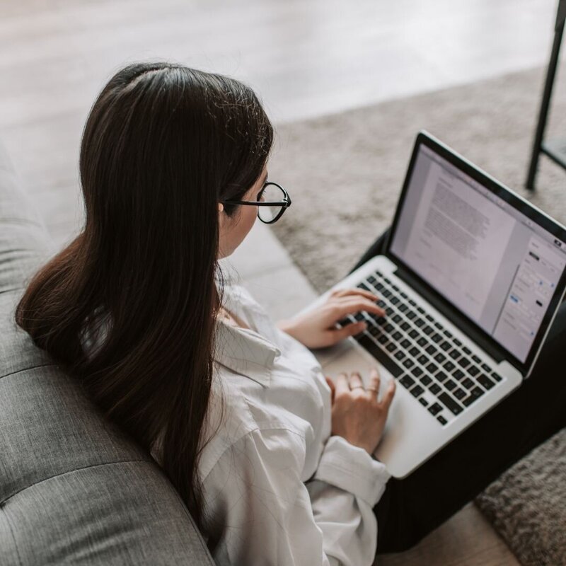 Woman with glasses working on a laptop while sitting on the floor
