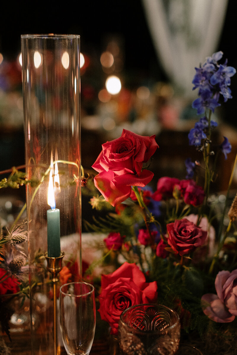 A colorful table arrangement featuring a lit candle, vibrant roses, and delicate flowers, creating an intimate and romantic atmosphere.
