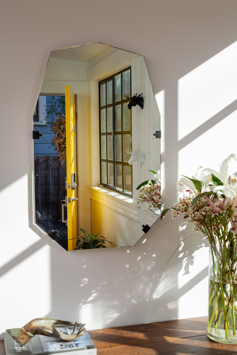 Interior brand photography of a mirror reflecting a yellow door and floral arrangement.
