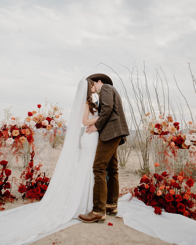 A couple kissing in the desert in West Texas, surrounded by a floral installation by Anthousai Floral Design;