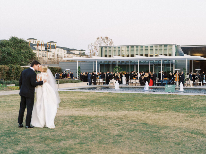 Bride and groom kissing with their reception and guests in the background