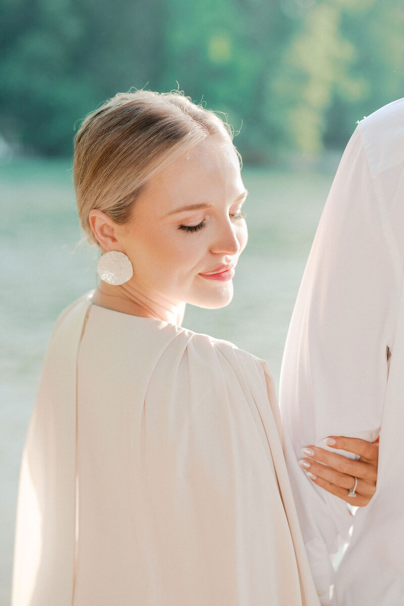 Bride in white dress with pearl earrings looks at Lake Lanier shoreline