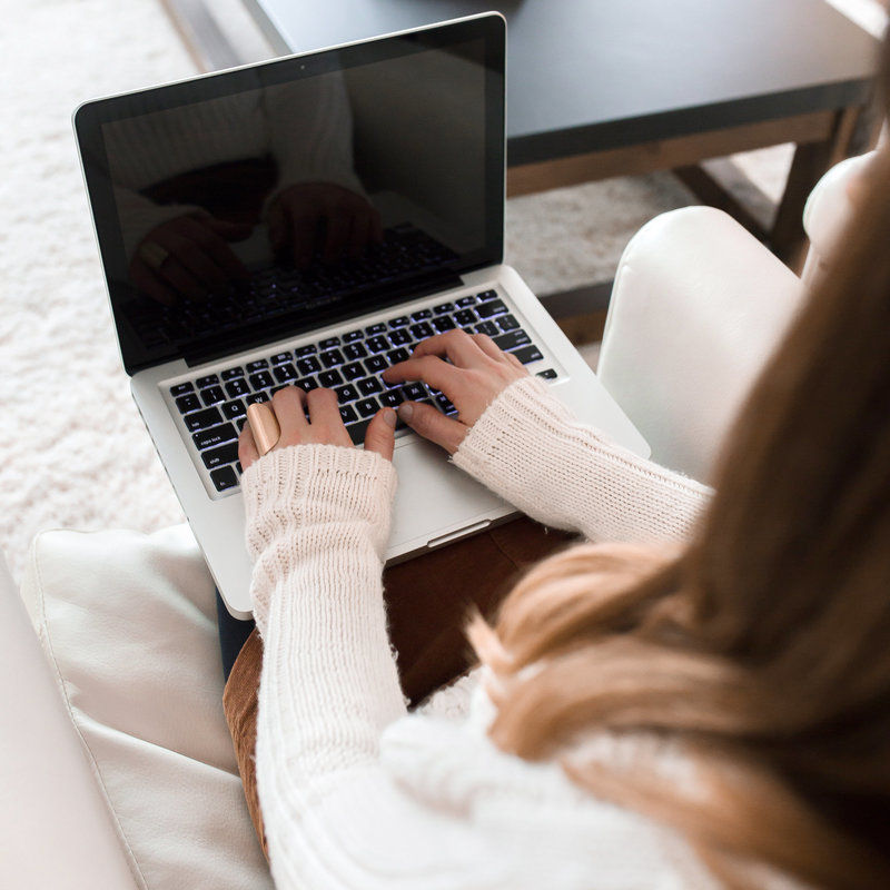 Frau sitzt auf einem Sessel und hat einen Laptop auf dem Schoß