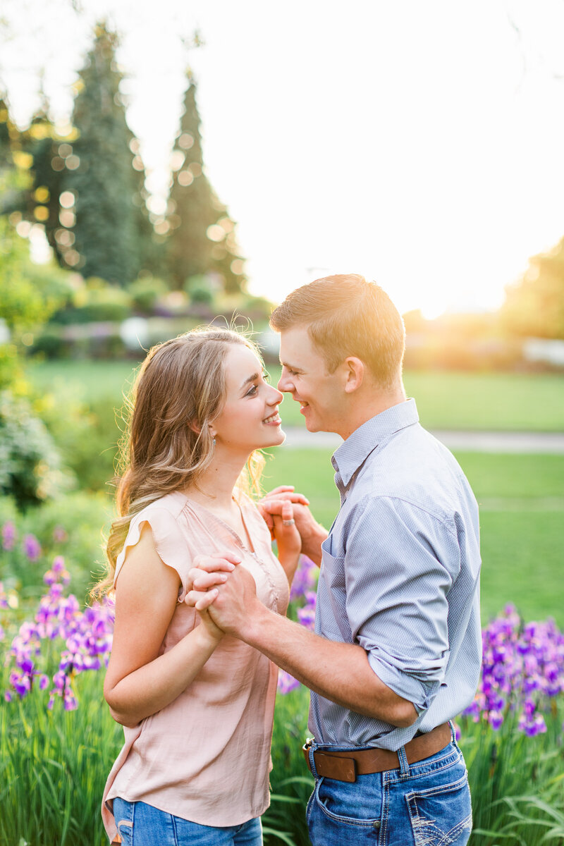 Young couple shares a kiss surrounded by summer blooms at Manito Park as golden sunlight filters through the trees.