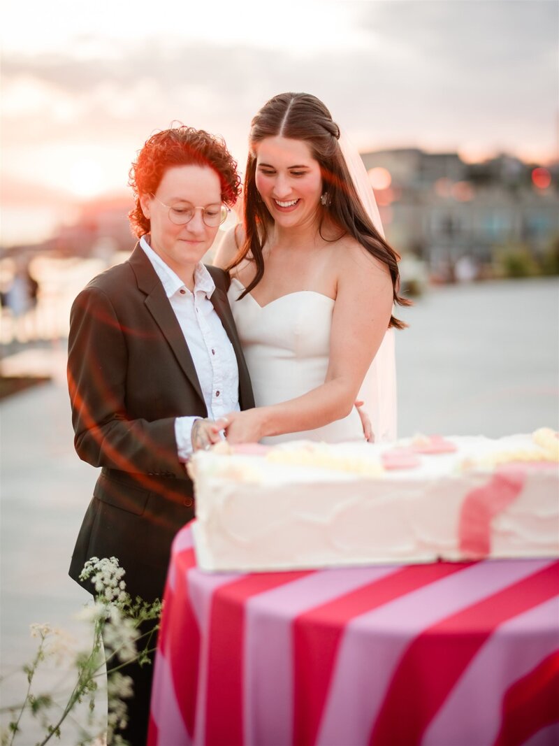A joyful couple cutting their gluten-free wedding cake at sunset, reflecting Grain Artisan Bakery’s commitment to celebrating love and diversity through inclusive, handcrafted desserts in Snohomish, WA.