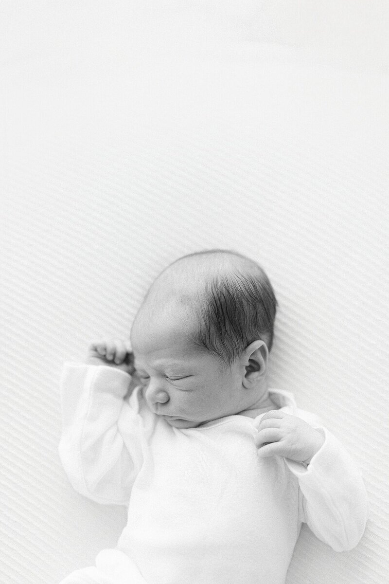 sleeping newborn in black and white lays on a white blanket in a white onsie during a session with Indianapolis newborn photographer Brittney Lear